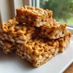 A stack of gooey, peanut butter-colored cheerio bars piled on a white plate.