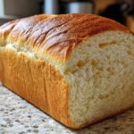 A freshly baked loaf of soft bread with a golden-brown crust, showing a tender, white crumb texture.