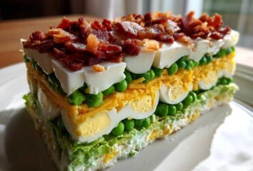 A tall, perfectly sliced portion of amazing 7 layer salad showing distinct layers of lettuce, peas, egg, cheese, and bacon topping.
