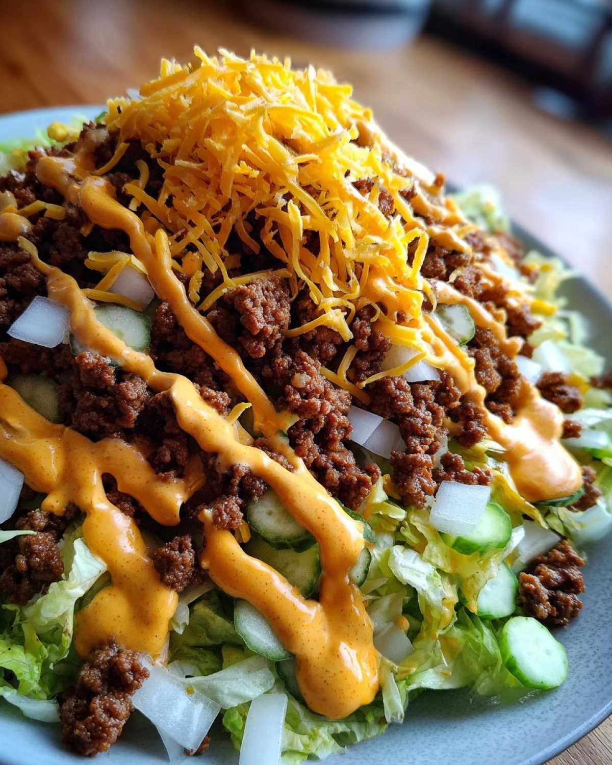 A close-up view of a healthy big mac salad piled high with seasoned ground beef, shredded cheese, and special sauce.
