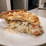 A close-up slice of amazing chicken pot pie recipe showing shredded chicken, carrots, peas, and corn in creamy sauce under a golden, flaky crust.