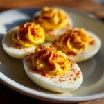 Four halves of perfectly prepared deviled eggs with piped yellow filling, dusted generously with paprika.
