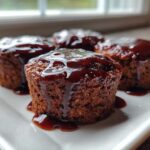 Four individual mini meatloaf portions topped with a thick, dark glaze, served on a white plate.