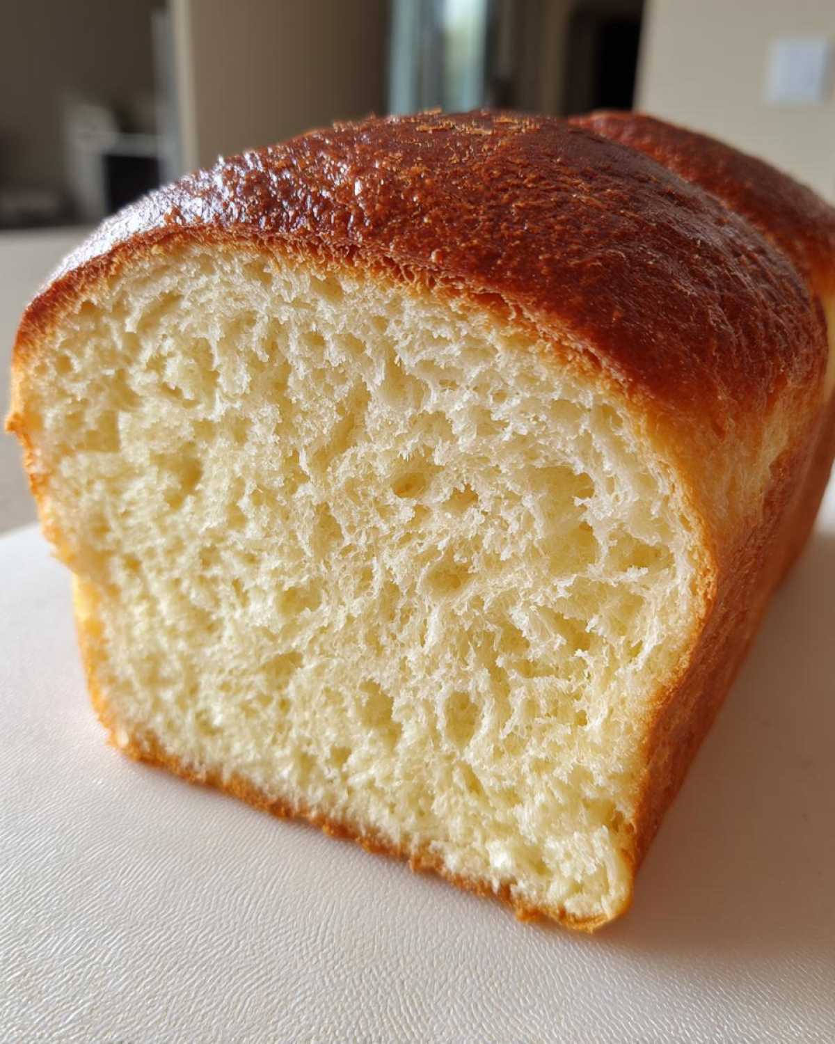 Close-up of a freshly baked loaf of soft bread showing the fluffy, light yellow interior crumb and a shiny, golden-brown crust.