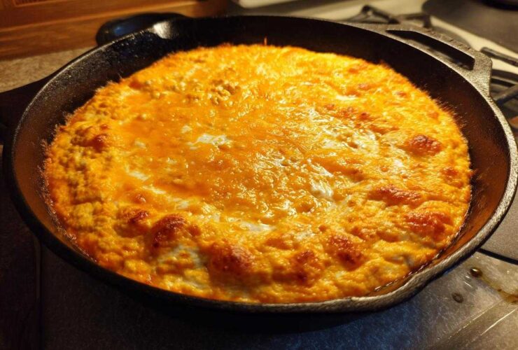 Hot, bubbly cottage cheese buffalo chicken dip topped with melted orange cheese in a black cast iron skillet.
