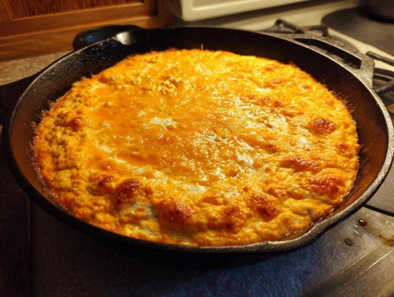 Hot, bubbly cottage cheese buffalo chicken dip topped with melted orange cheese in a black cast iron skillet.