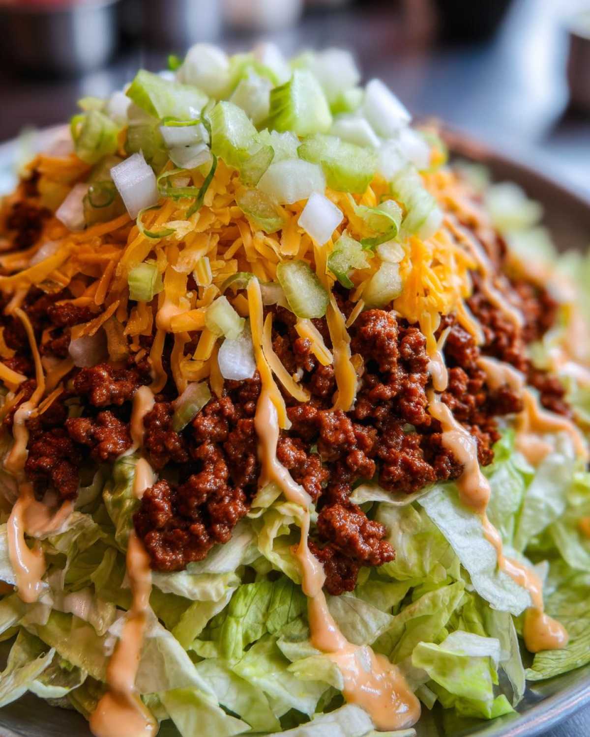 A close-up view of a big mac salad featuring shredded lettuce, seasoned ground beef, shredded cheese, diced pickles/onions, and special sauce drizzle.