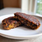 Two halves of a dark, richly seared black bean burger resting on a white plate, showing the textured interior.