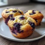 Three golden-brown blueberry cottage cheese muffins with visible blueberries, resting on a light gray plate.