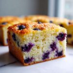 A close-up of a thick, fluffy square slice of blueberry sheet pan pancakes with a golden top.