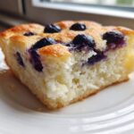 Close-up of a fluffy, golden slice of blueberry sheet pan pancakes served on a white plate.