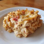 A close-up of a creamy, cheesy serving of chicken spaghetti casserole with shredded chicken and a browned topping.