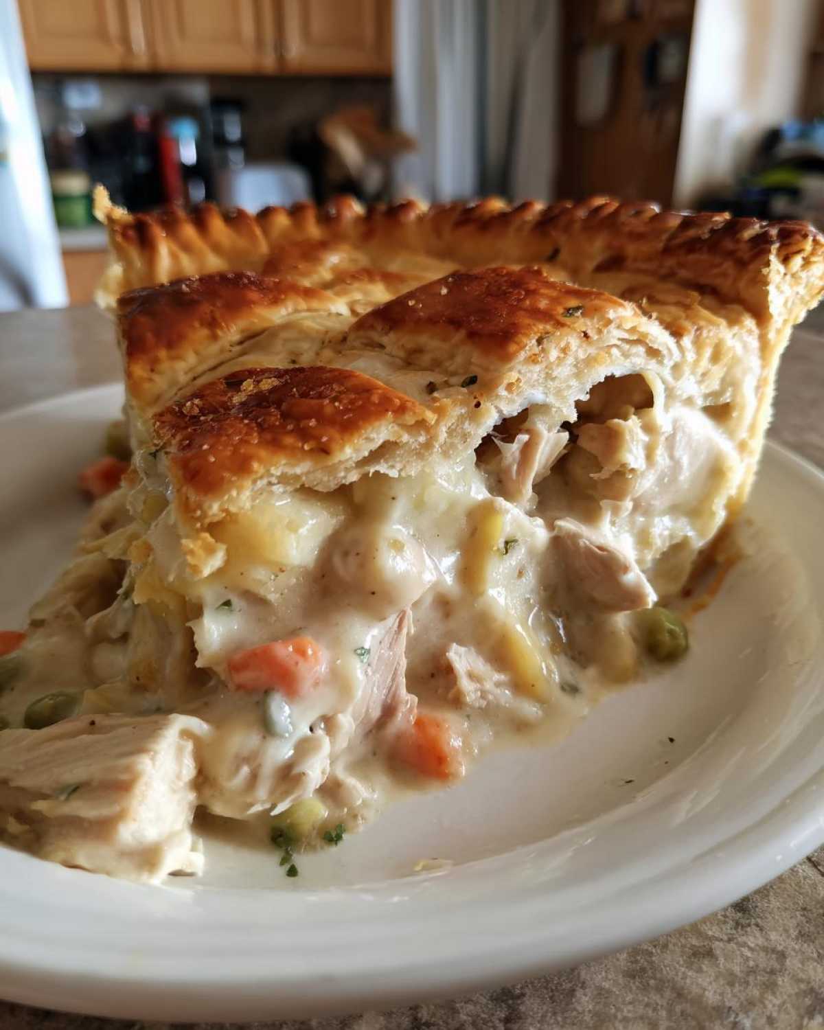 A close-up slice of chicken pot pie recipe showing flaky crust and creamy filling with visible chicken, carrots, and peas.