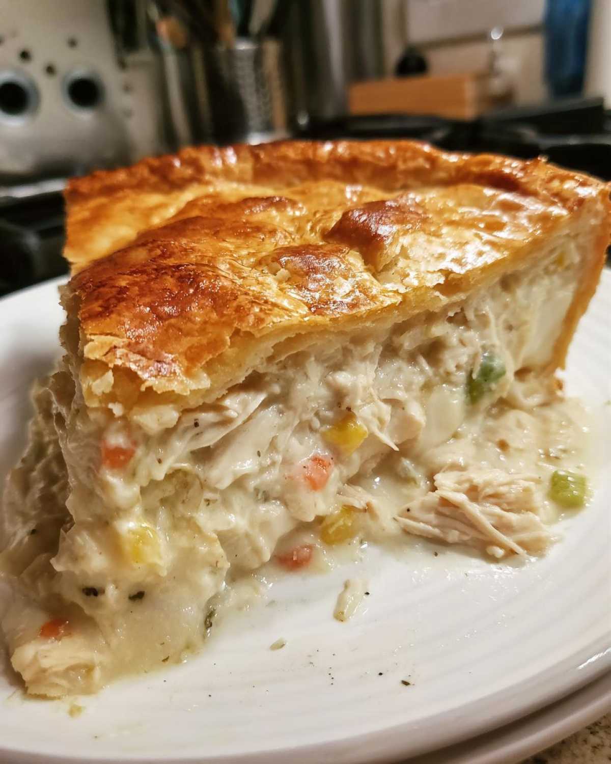 A close-up of a thick slice of chicken pot pie recipe showing creamy filling, shredded chicken, vegetables, and golden crust.