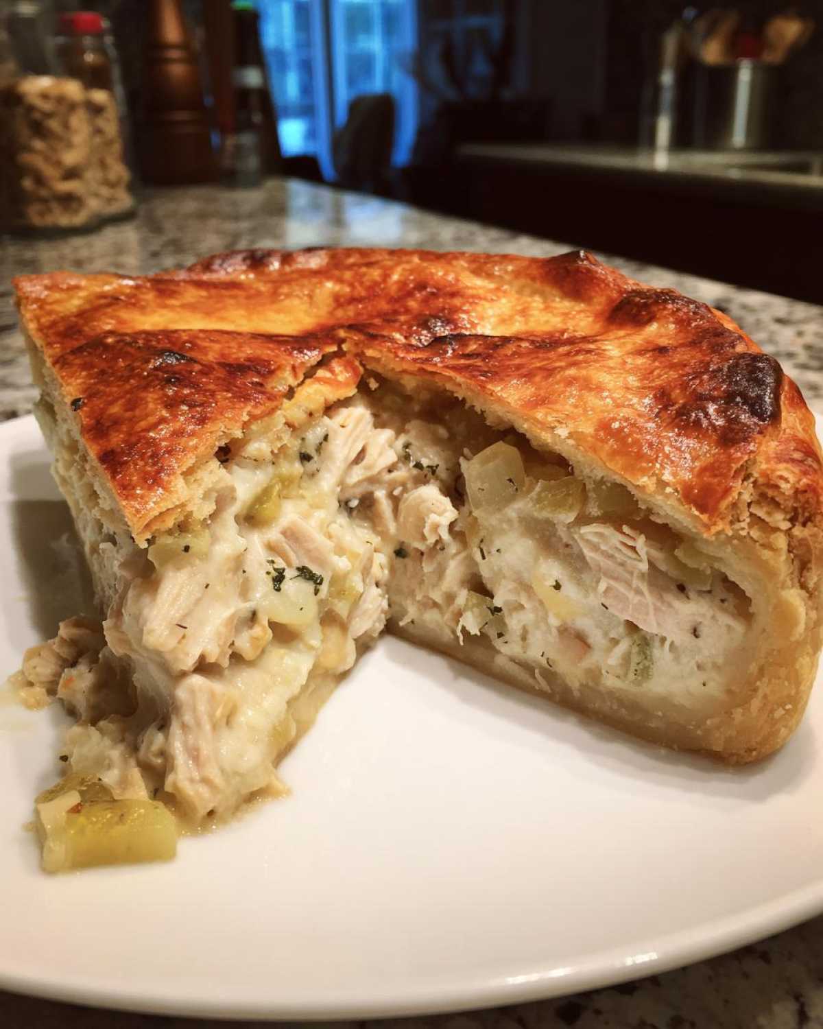 A thick slice of chicken pot pie recipe showing a flaky, golden crust and creamy filling packed with shredded chicken and vegetables.
