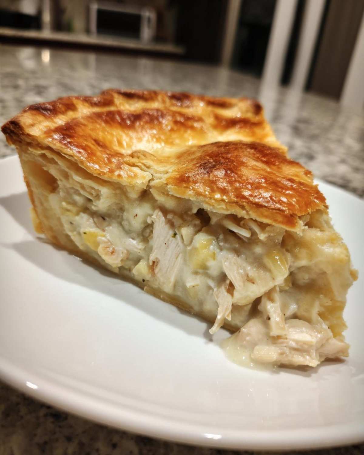 A thick slice of chicken pot pie recipe with flaky, golden crust and creamy filling showing shredded chicken.