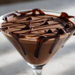 A close-up of a rich, creamy chocolate martini topped with drizzled chocolate syrup.