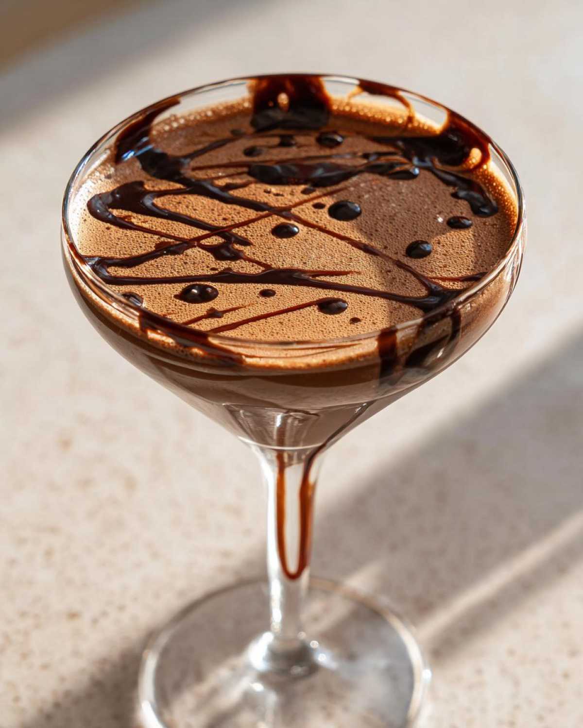 Close-up of a creamy chocolate martini in a coupe glass, drizzled with dark chocolate syrup.