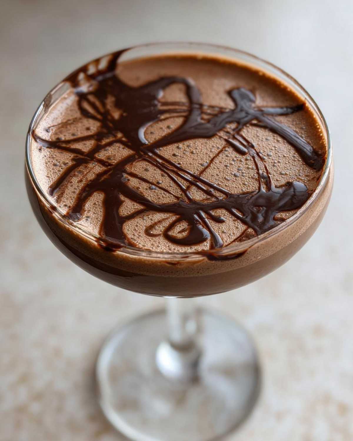 Close-up overhead view of a creamy chocolate martini topped with drizzled dark chocolate syrup.