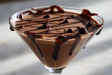 A close-up of a rich, creamy chocolate martini topped with drizzled chocolate syrup.