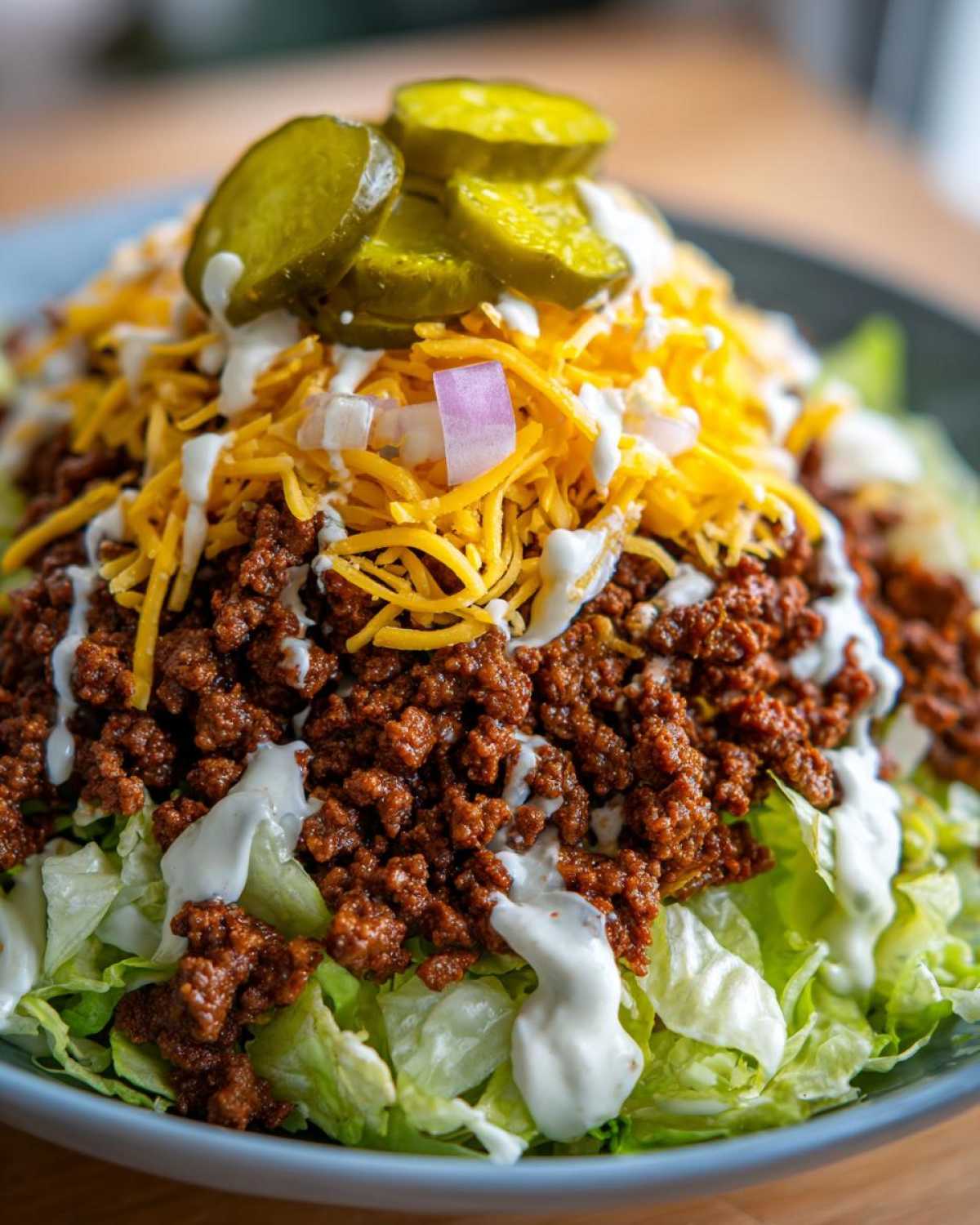 A close-up of a delicious big mac salad piled high with seasoned ground beef, shredded cheese, white sauce, and pickle slices.