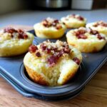 Close-up of Copycat Café-Style Bacon Gruyere Egg Bites in a muffin tin, one bite has a piece taken out.