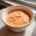 Close-up of creamy orange Copycat Classic Burger Spread Sauce with visible green relish flecks in a white bowl.