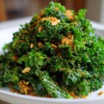A mound of vibrant green kale tossed and topped with crunchy golden breadcrumbs and seeds, resembling Copycat Kale Crunch Salad.