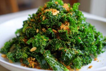 A mound of vibrant green kale tossed and topped with crunchy golden breadcrumbs and seeds, resembling Copycat Kale Crunch Salad.