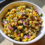 A close-up of vibrant Copycat Mexican Grill Corn Salsa featuring charred corn kernels, diced red onion, and cilantro in a white bowl.