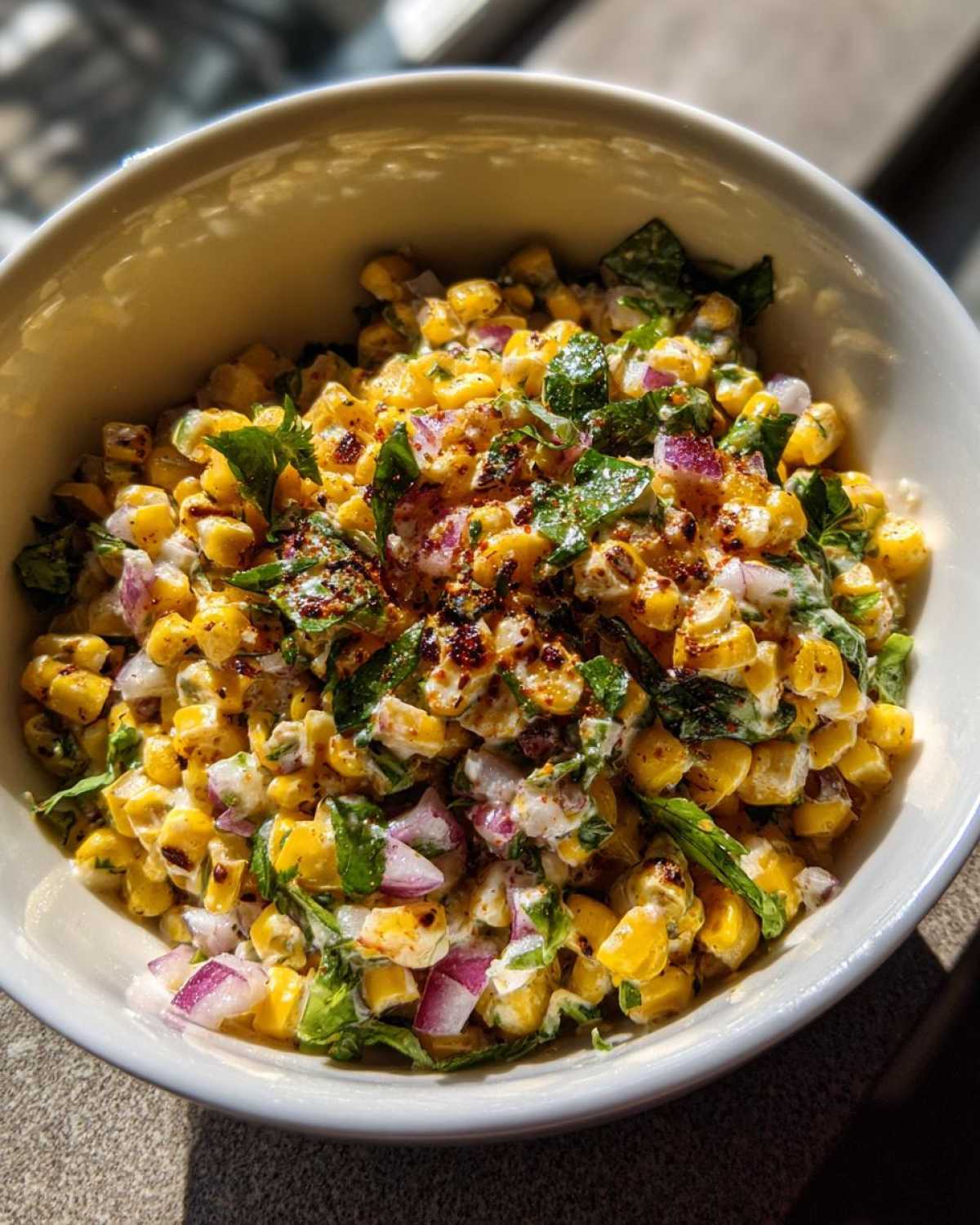 Close-up of a white bowl filled with Copycat Mexican Grill Corn Salsa featuring charred corn, red onion, and cilantro.