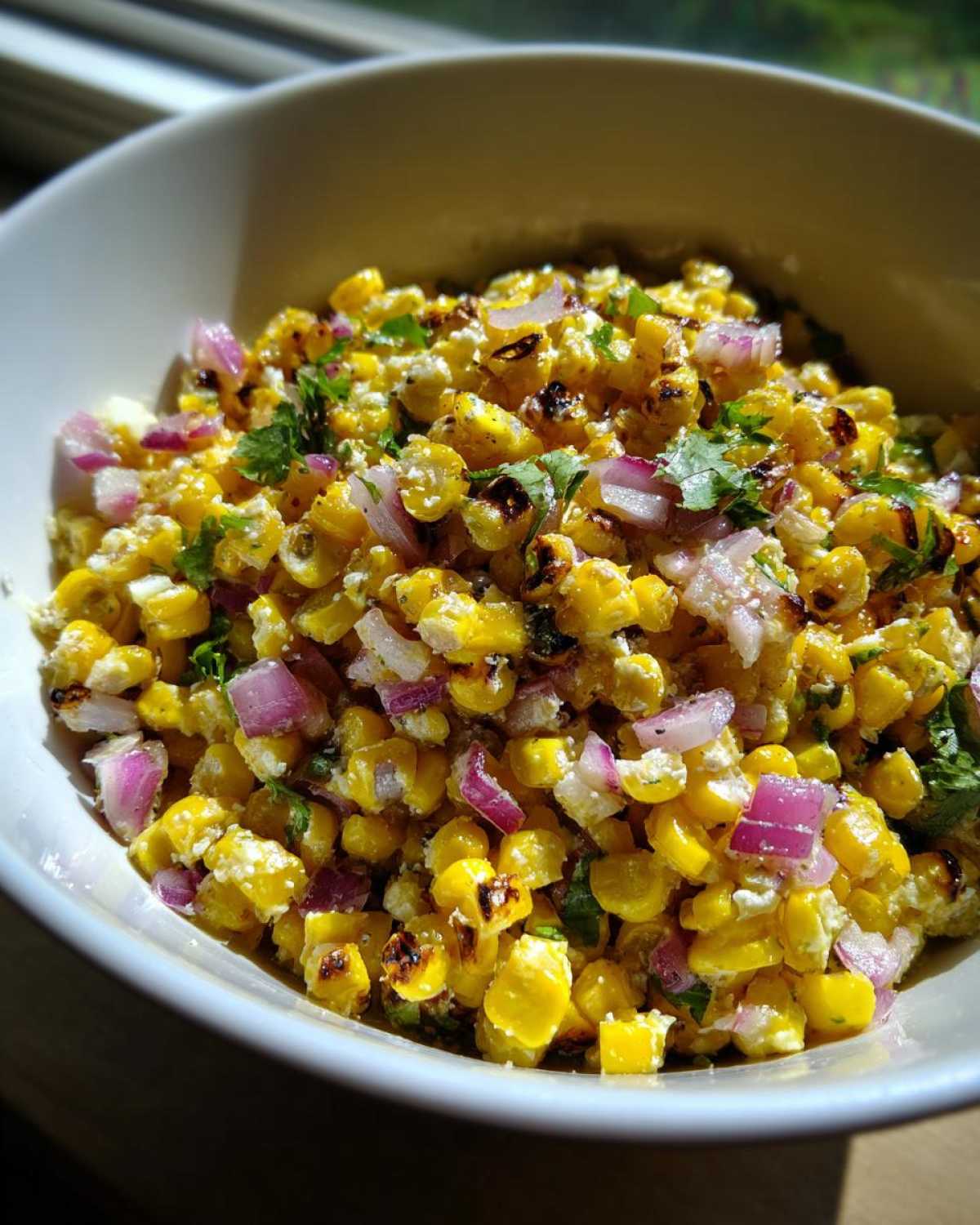 Close-up of charred corn kernels mixed with red onion and cilantro in a white bowl, showcasing the Copycat Mexican Grill Corn Salsa.