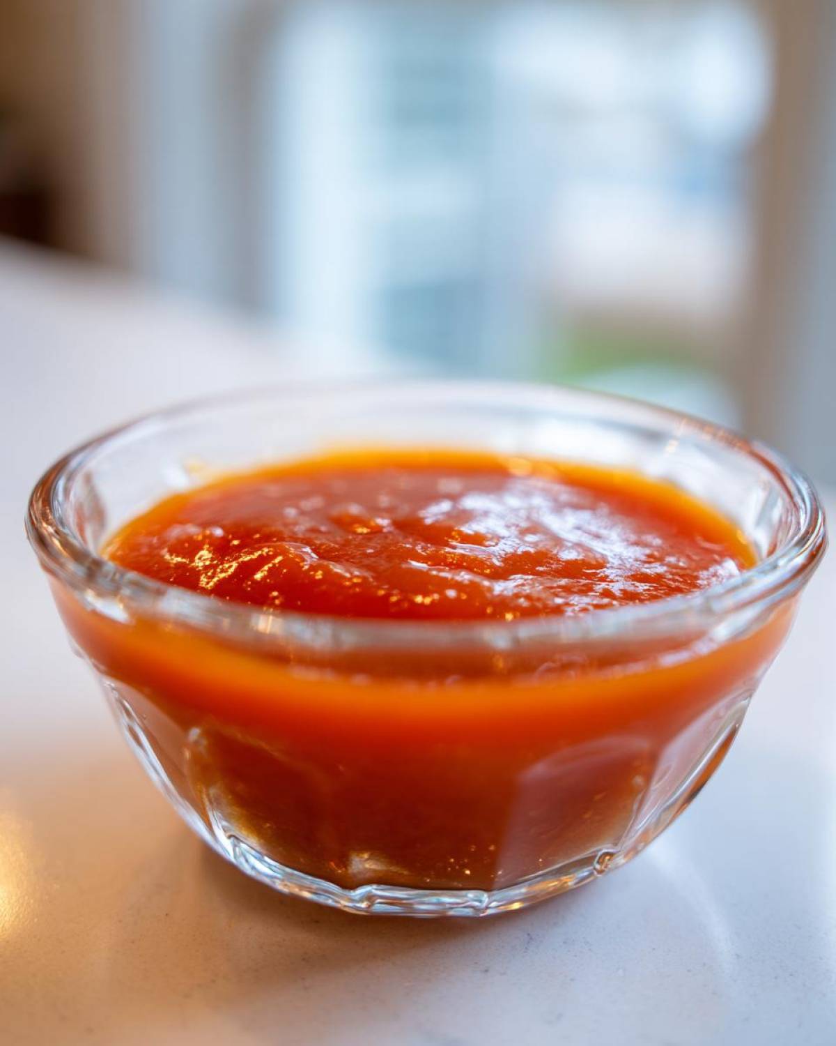 Close-up of bright orange Copycat Sweet-Tangy Polynesian Dipping Sauce served in a small, clear glass bowl.