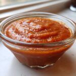 Close-up of thick, vibrant orange Copycat Sweet-Tangy Polynesian Dipping Sauce in a small glass bowl.