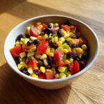 A close-up of a vibrant bowl of cowboy caviar recipe featuring black beans, corn, and diced tomatoes.