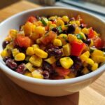 Close-up of a white bowl filled with colorful cowboy caviar recipe featuring black beans, corn, tomatoes, and peppers.