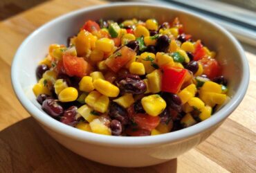 Close-up of a white bowl filled with colorful cowboy caviar recipe featuring black beans, corn, tomatoes, and peppers.