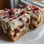 Two decadent slices of cranberry bliss bars topped with thick white frosting, a white chocolate drizzle, and dried cranberries.