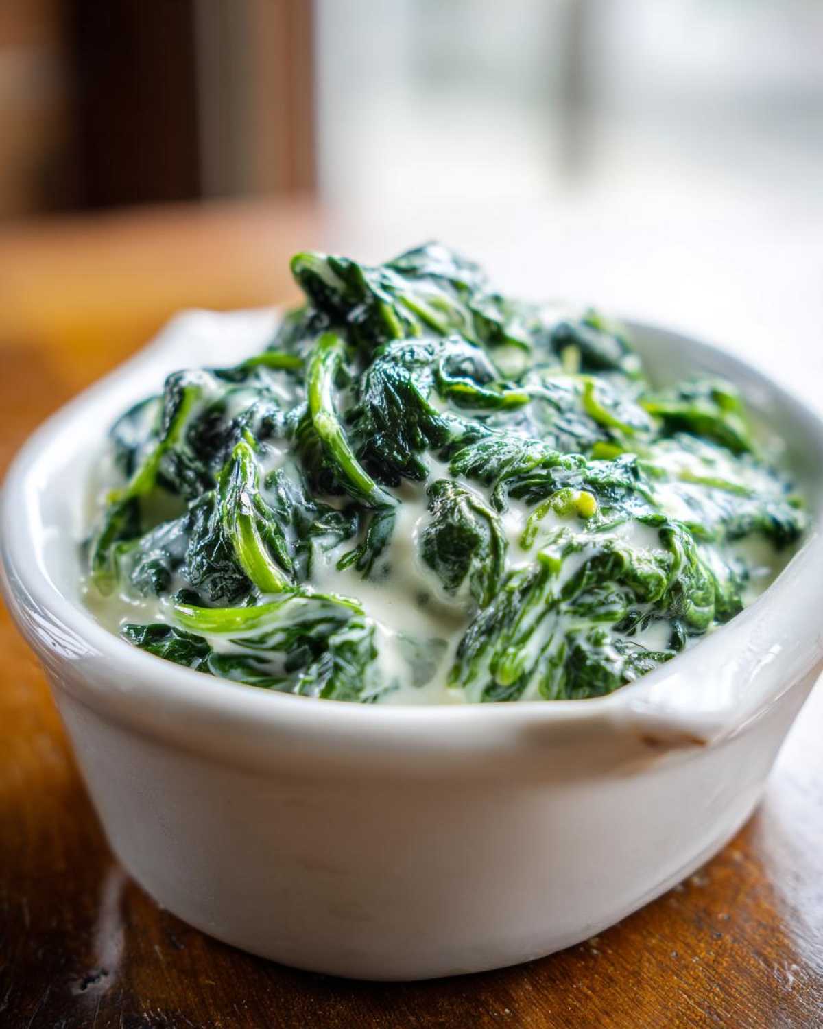 Close-up of rich, dark green creamed spinach served in a small white ceramic bowl.