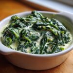 Close-up of rich, dark green creamed spinach served hot in a small white ceramic bowl.