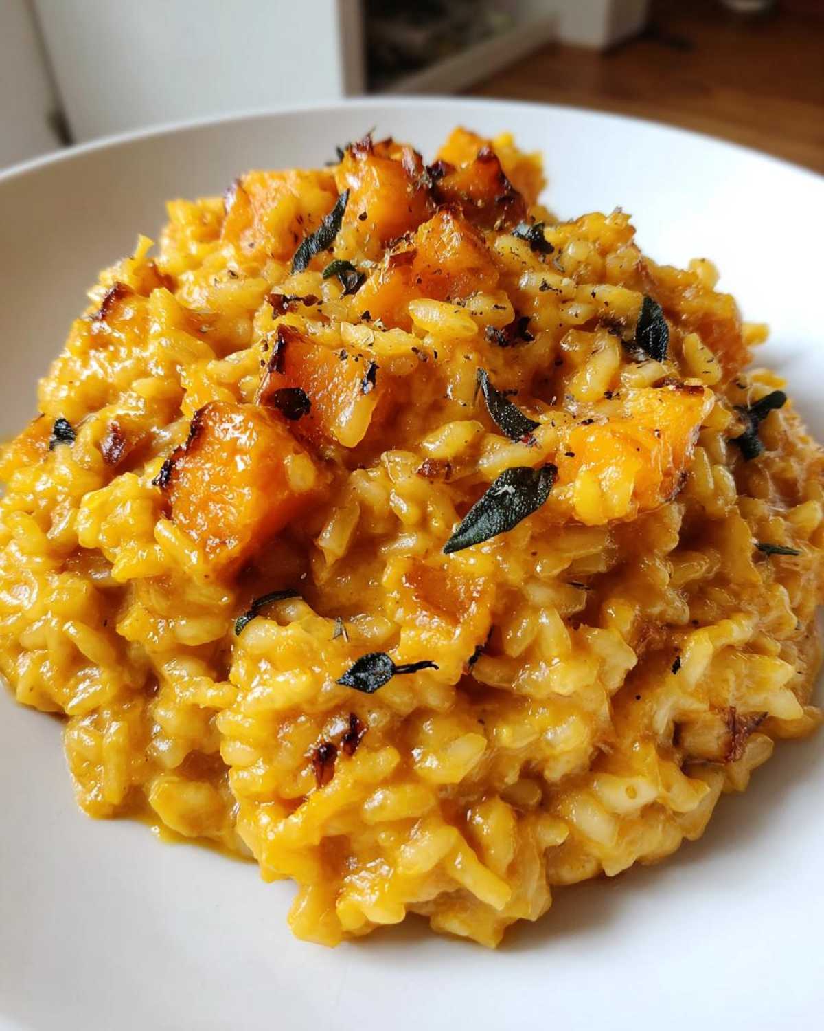 A close-up view of creamy butternut squash risotto topped with roasted squash cubes and crispy sage leaves.