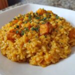 A close-up of creamy butternut squash risotto topped with roasted squash cubes and fresh herbs.