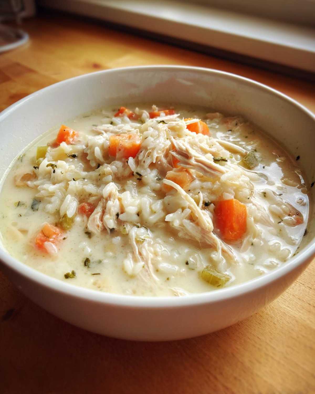 Close-up of a bowl of creamy chicken and rice soup with shredded chicken, carrots, and celery.