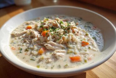 Close-up of a hearty bowl of creamy chicken and rice soup, topped with shredded chicken and fresh parsley.