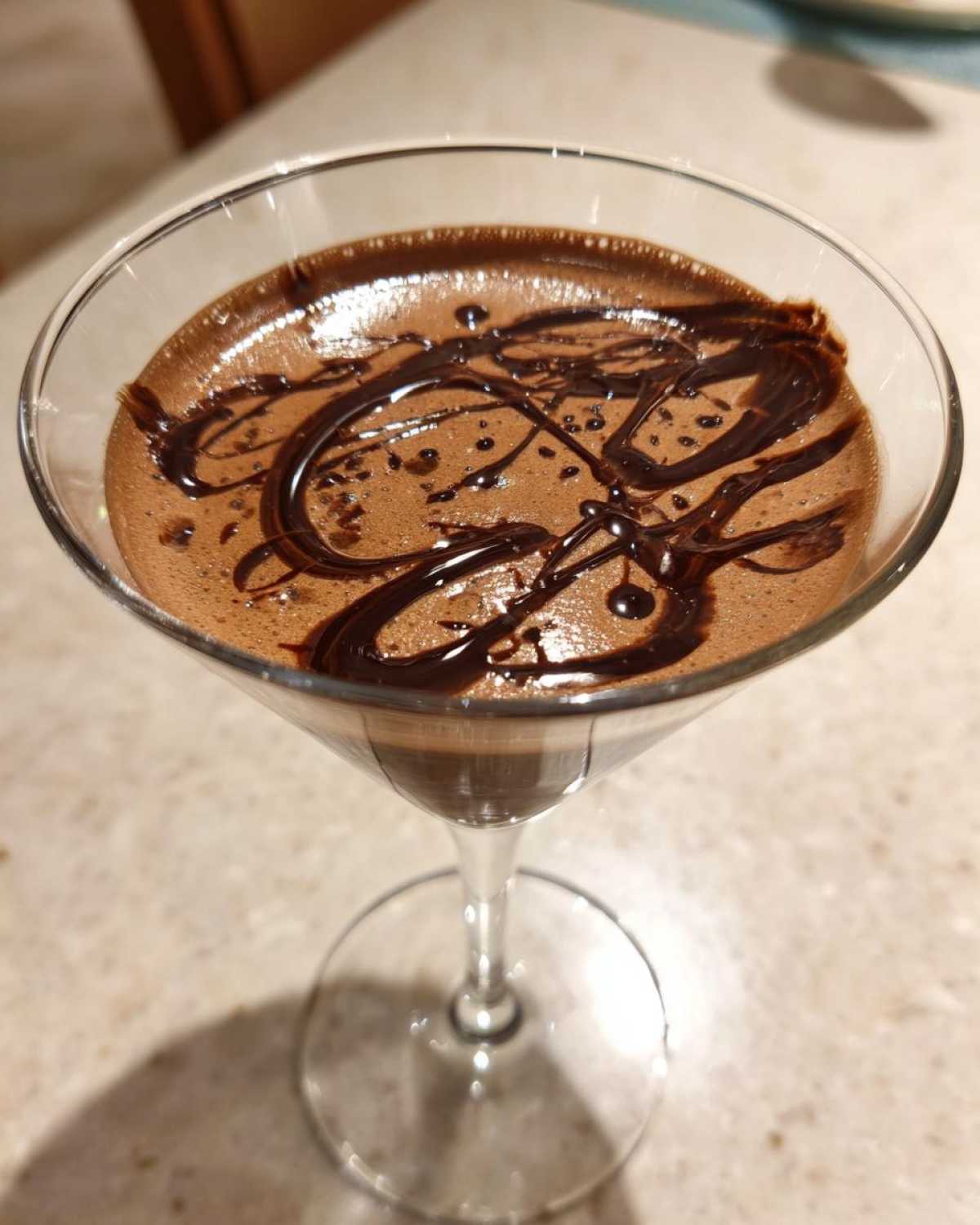 Close-up of a creamy chocolate martini in a coupe glass, garnished with a dark chocolate syrup drizzle.