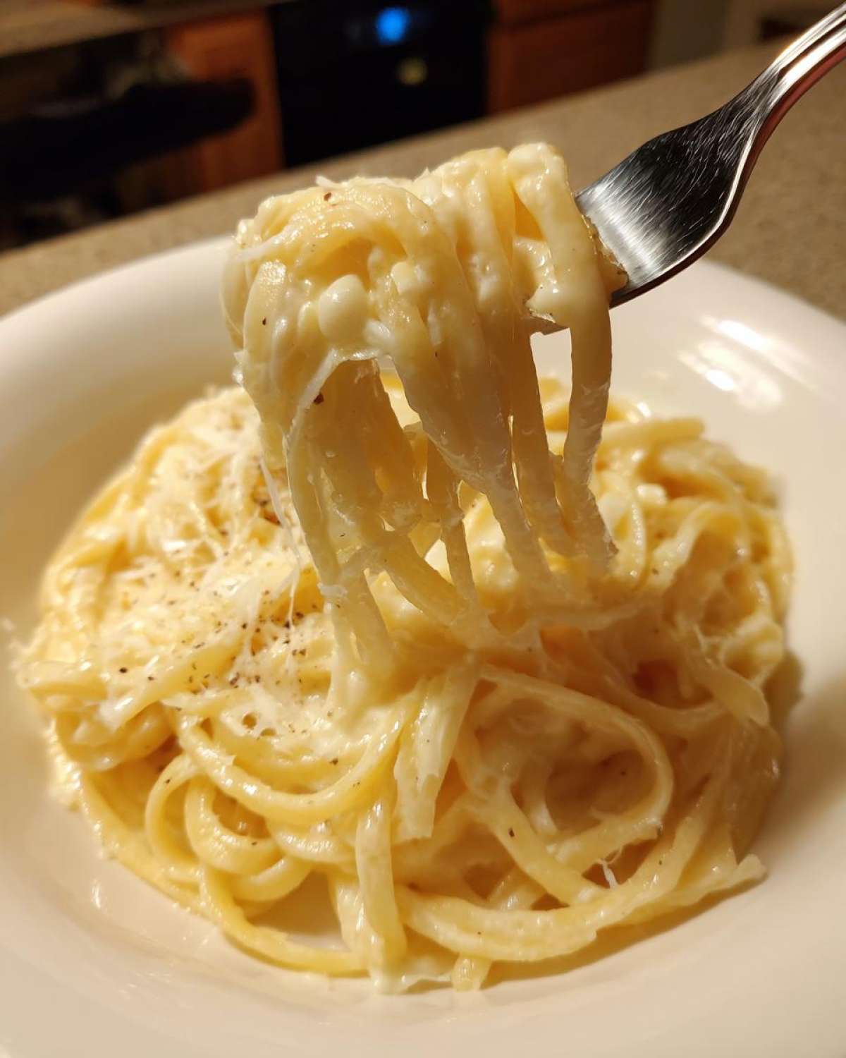 A fork lifting fettuccine coated in creamy Easy Cottage Cheese Alfredo Sauce, topped with grated cheese.