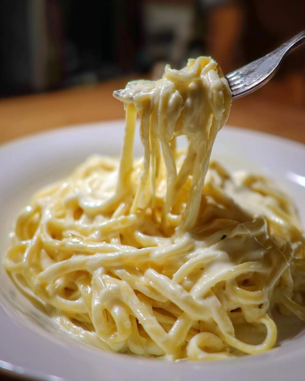 Close-up of fettuccine pasta coated in creamy Easy Cottage Cheese Alfredo Sauce being lifted by a fork.
