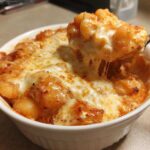 A spoonful of Creamy Roasted Garlic Tomato Gnocchi Bake being lifted from a white bowl, showing melted, stringy cheese.