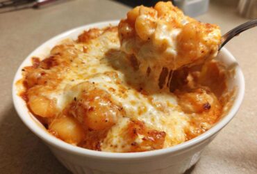 A spoonful of Creamy Roasted Garlic Tomato Gnocchi Bake being lifted from a white bowl, showing melted, stringy cheese.