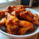 A close-up of crispy, saucy buffalo wings piled high in a white serving bowl.